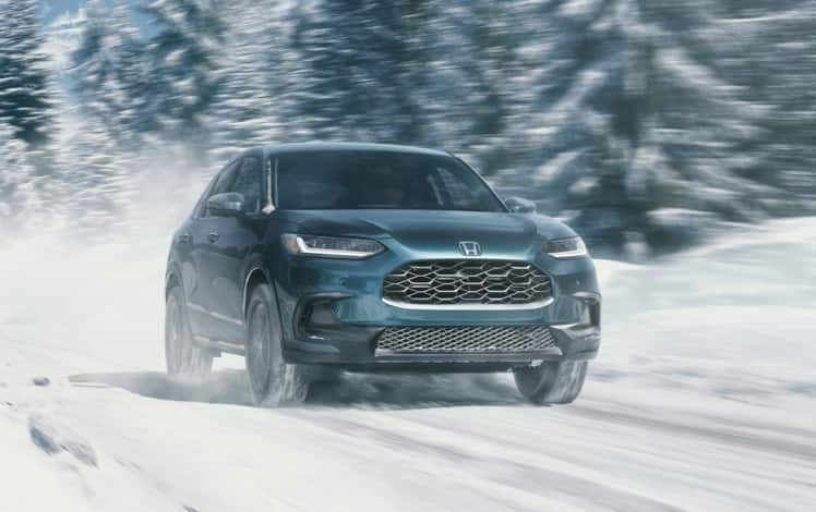 Front passenger-side view of the 2025 Honda HR-V EX-L in Nordic Forest Pearl, driving on a snowy forested trail.